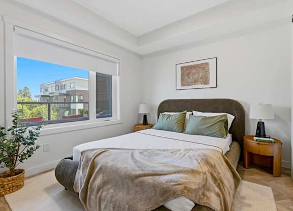 A bedroom with a large bed and a view of a building outside the window.