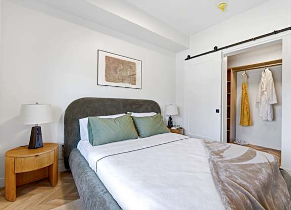 A bedroom with a bed, a nightstand with a lamp, and a closet with clothes.