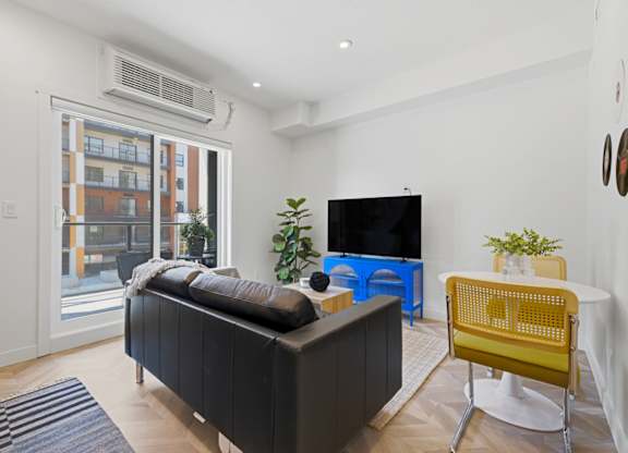 A living room with a black sofa, a yellow chair, and a flat screen TV.