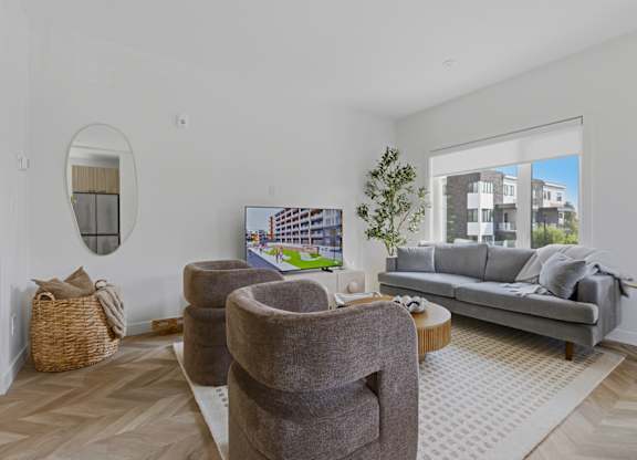 A living room with a grey couch, a round mirror, and a coffee table.