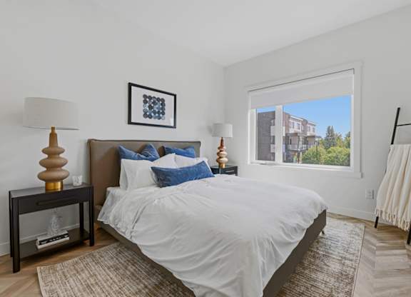A bedroom with a large bed and a view of a building outside the window.
