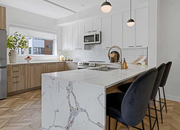 A modern kitchen with a marble island and black chairs.
