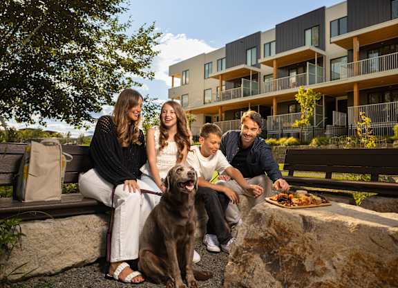 A group of people are sitting on a bench with a dog in front of them.