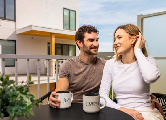 A man and a woman are sitting at a table with LEGO mugs in front of a modern building.