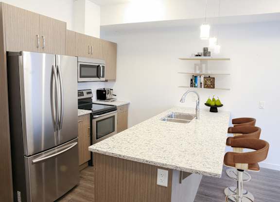 A kitchen with a refrigerator, microwave, oven, sink, and bar stools.