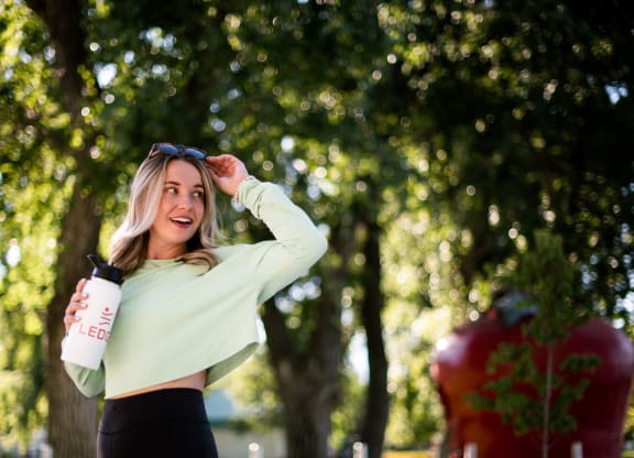 a woman standing in a park holding a bottle of water