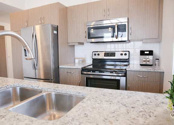 A kitchen with a stainless steel refrigerator, microwave, oven, and sink.