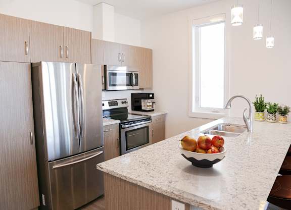A modern kitchen with a refrigerator, microwave, oven, and sink.