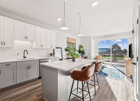 A kitchen with white cabinets and a white island with brown chairs.