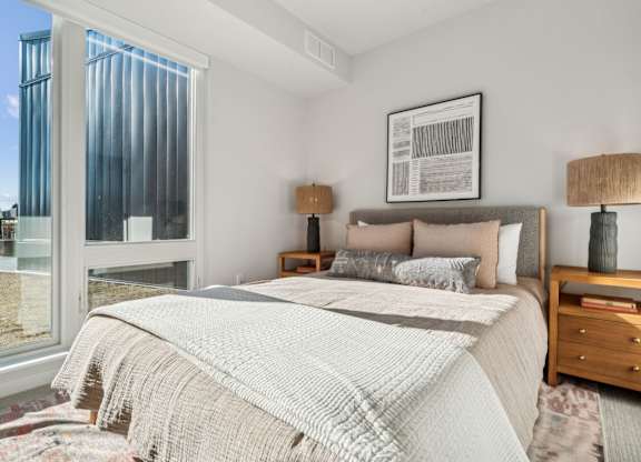 A bedroom with a large bed and a window overlooking a cityscape.