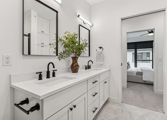 A white bathroom with a large mirror and a plant on the sink.