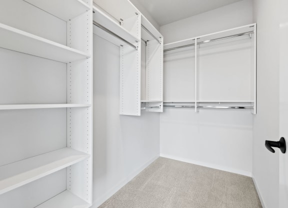 a walk in closet with white walls and shelves and a black door