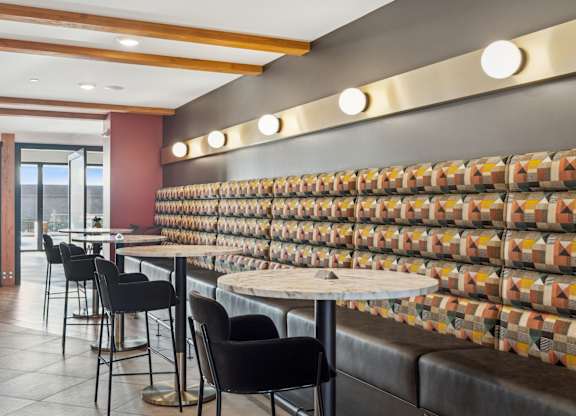 A restaurant with a long table and chairs with a wall of tiles behind it.