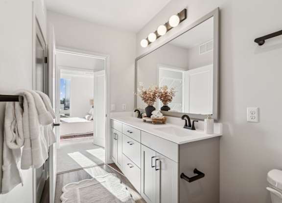 A bathroom with a white vanity and a mirror with lights above it.