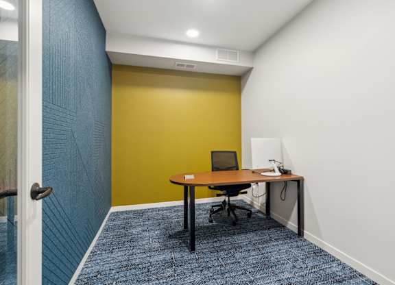 A room with a yellow wall and a desk with a laptop on it.