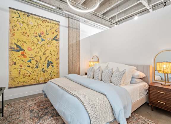 A bedroom with a large floral print on the wall and a bed with a blue comforter.