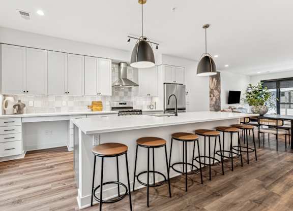 A kitchen with white cabinets and a white island with four stools.
