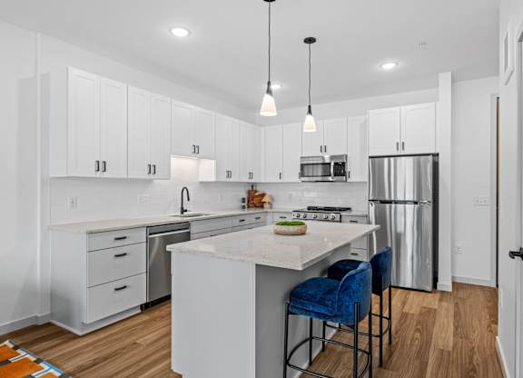 A kitchen with white cabinets and a white island with blue chairs.