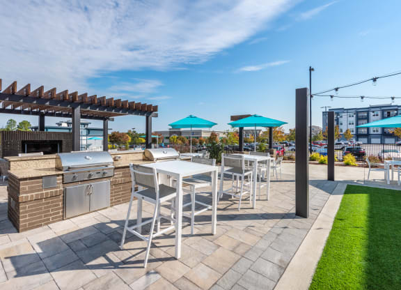 a patio with a grill and tables with chairs and umbrellas