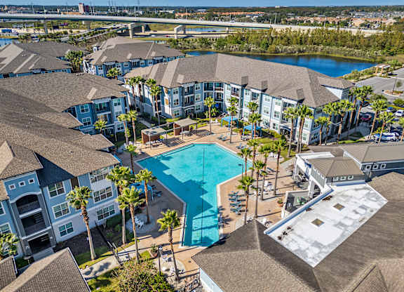A large swimming pool is surrounded by palm trees and apartment buildings.