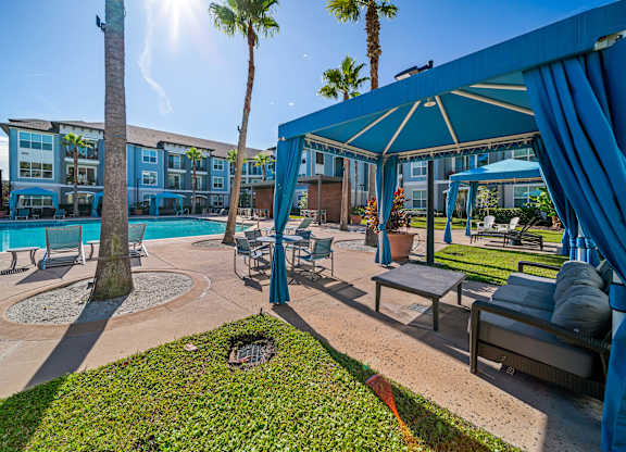 A sunny day at the poolside with a blue umbrella and chairs.