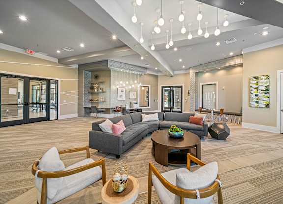 A spacious living room with a grey couch, wooden chairs, and a coffee table.