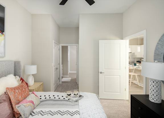 A bedroom with a bed, a painting, a ceiling fan, and a door leading to another room.