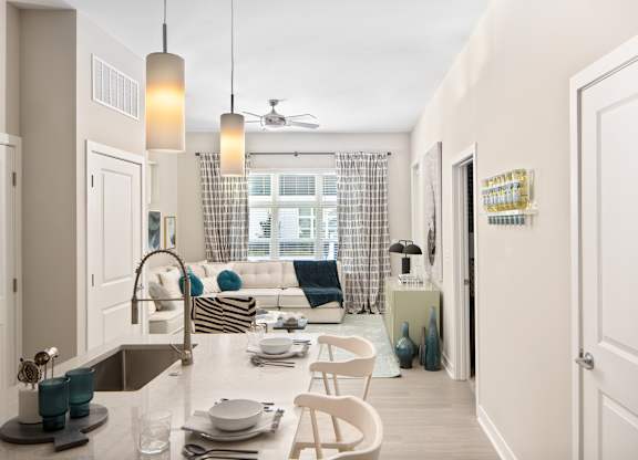 A kitchen with a sink, a dining table with chairs, and a window with curtains.