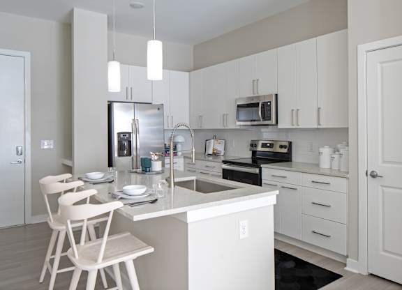 A kitchen with white cabinets and a white island with a chair.