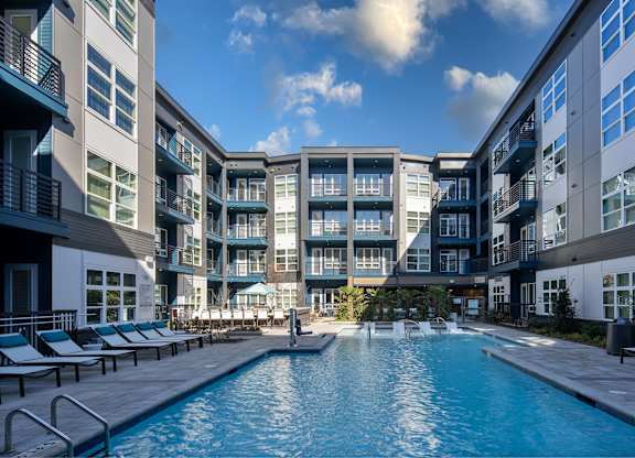 A swimming pool in front of a building with lounge chairs around it.