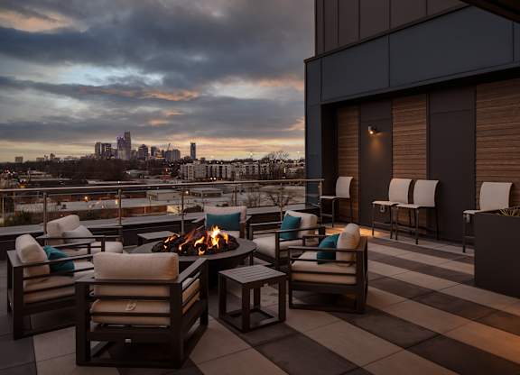 A rooftop patio with a fire pit and chairs.
