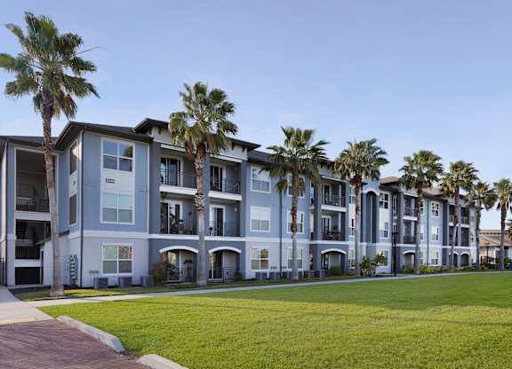 A row of modern apartment buildings with palm trees in front.