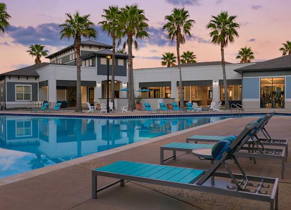 A poolside area with lounge chairs and a building in the background.