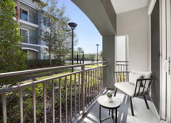 A balcony with a chair and table is overlooking a green area.