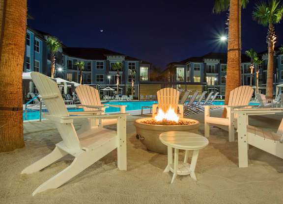 A fire pit sits in the middle of a sandy area with chairs around it.