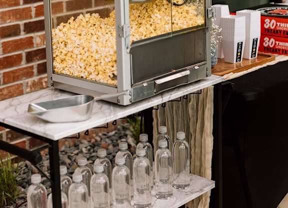 A red popcorn machine is on a table with bottles of water.