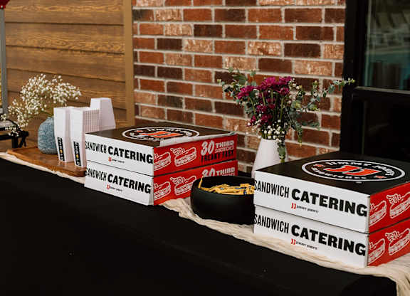 A table with a black cloth and several boxes of Sandwich Catering on it.