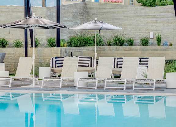 A pool with chairs and umbrellas is surrounded by a wall.