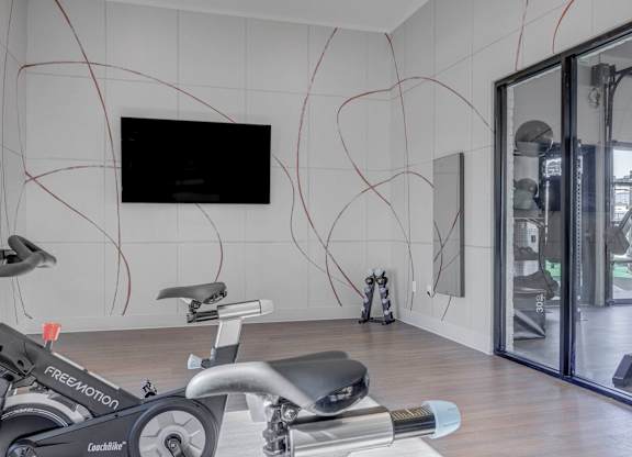 A room with a treadmill and a television on the wall.