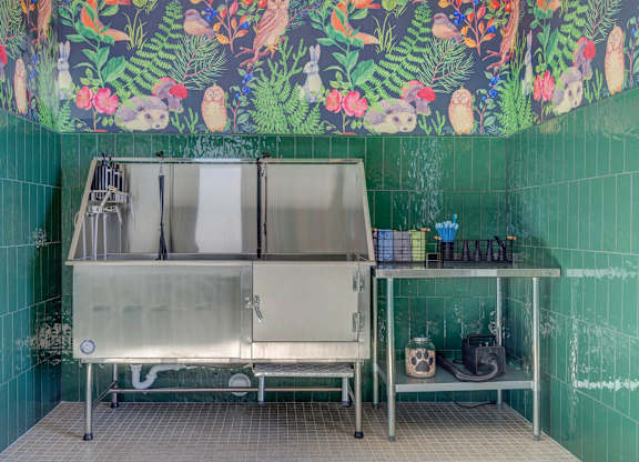 A stainless steel sink in a room with green tiled walls.