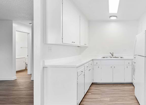 A white kitchen with a sink and a refrigerator.