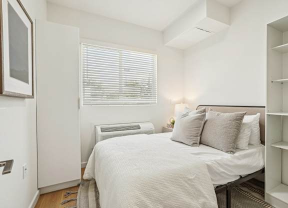 A white bedroom with a bed, pillows, and a window with blinds.