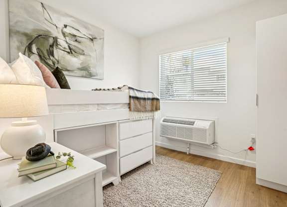 A white room with a bed, a dresser, a nightstand, and a window with blinds.