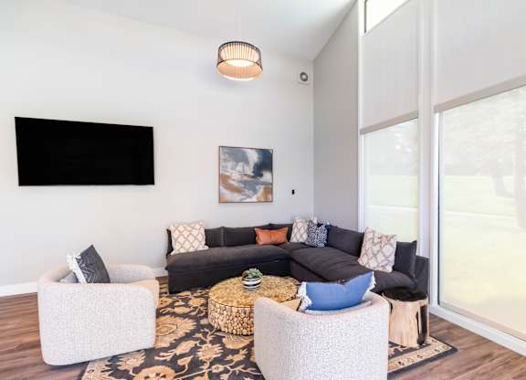 A living room with a black couch and a television on the wall. at Chaparral Apartments, California