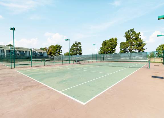 A tennis court with a net and a green fence. at Chaparral Apartments, Palmdale