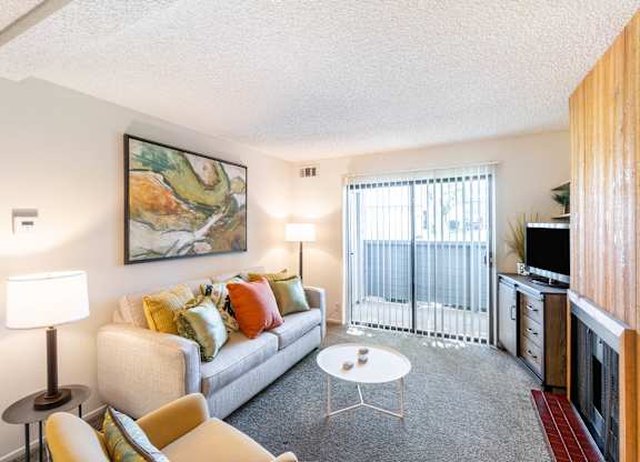 A living room with a couch, chairs, and a painting on the wall at Chaparral Apartments, California