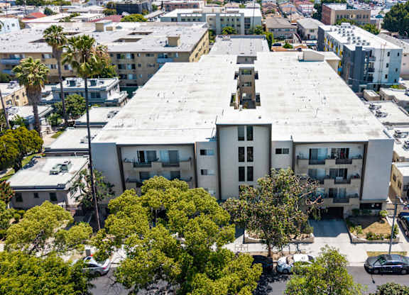 A large building with a flat roof is surrounded by trees and other buildings.