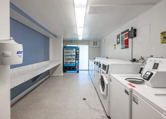 A laundromat with a row of washers and dryers at Oak Park Apartments, Monrovia, 91016