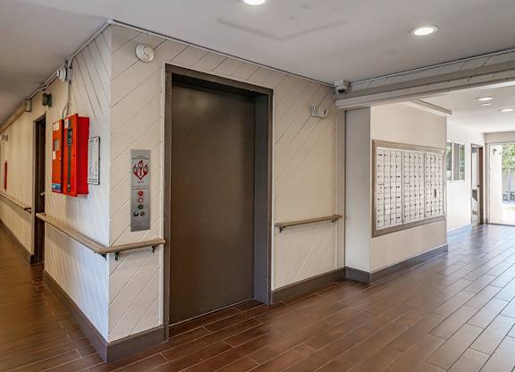 A hallway with a black door and a red fire extinguisher on the wall at Oak Park Apartments, Monrovia, 91016