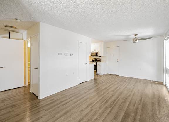 A room with white walls and wooden flooring with a ceiling fan.